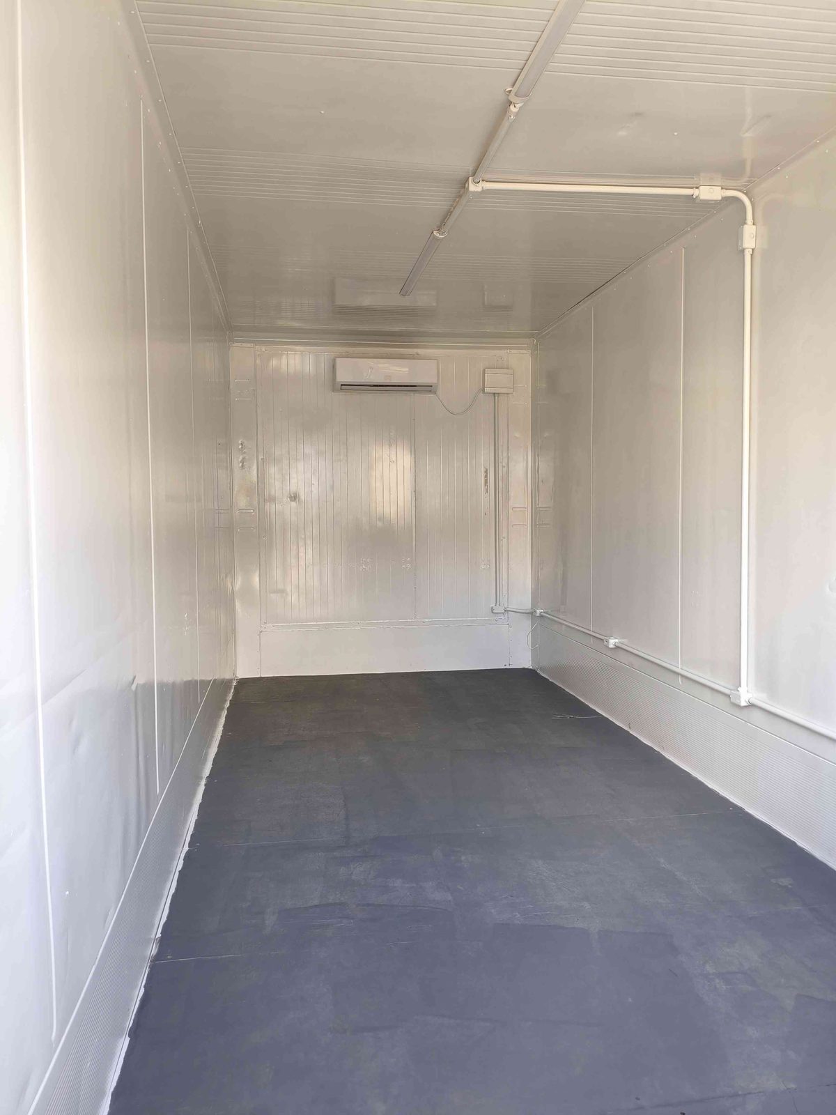 Interior do container escritório com paredes em painel branco, piso cinza e ar-condicionado
