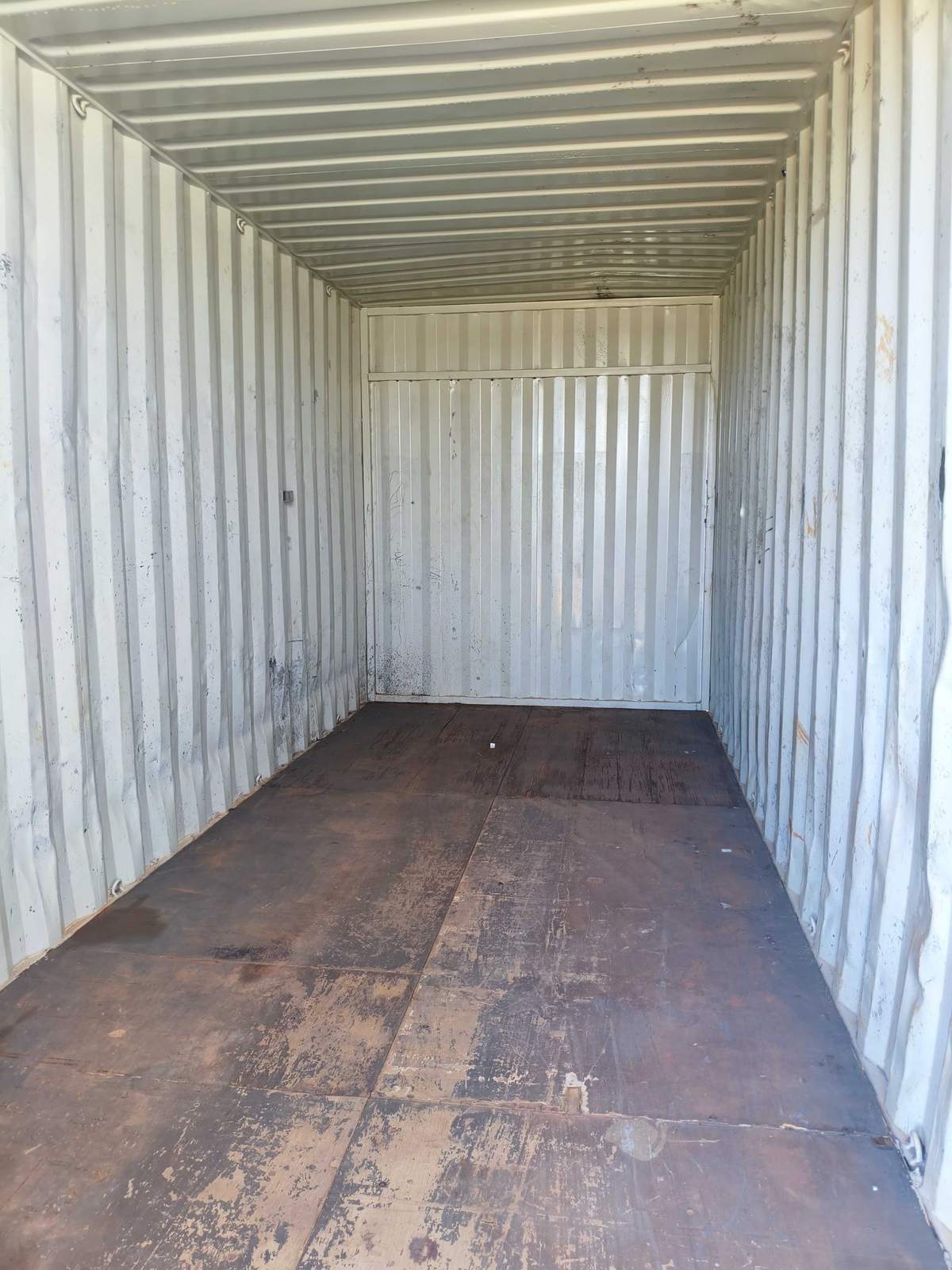 Interior do container depósito com piso de madeira e paredes brancas