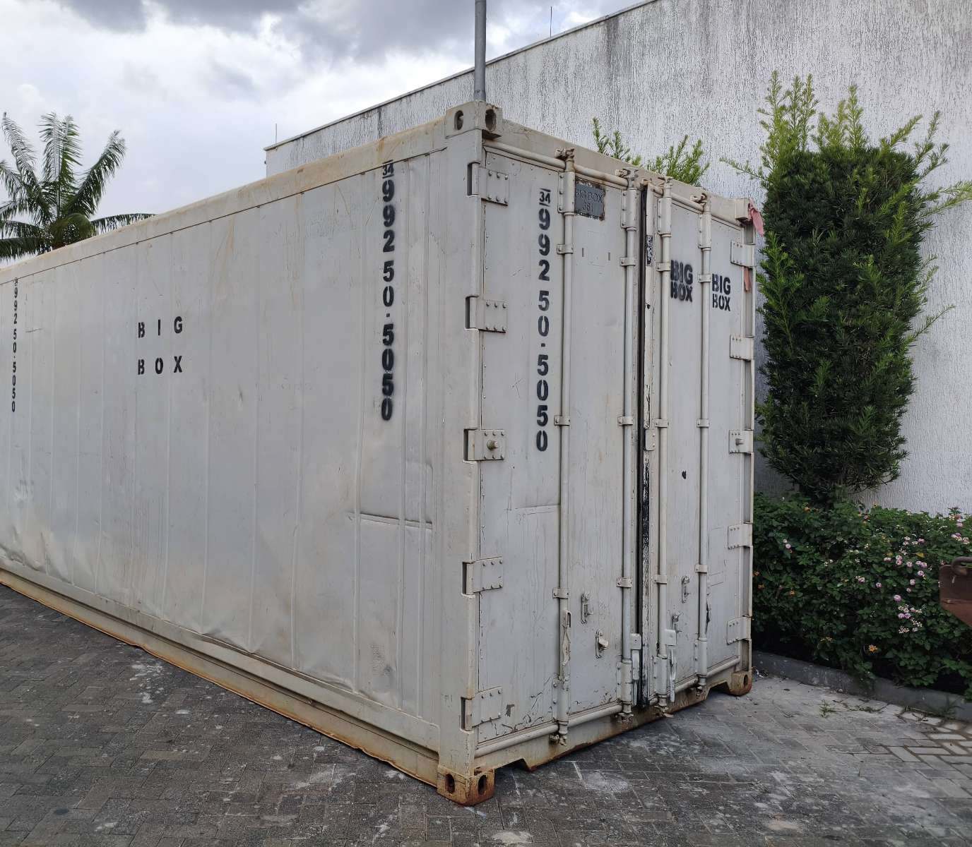 Container reefer branco posicionado sobre piso intertravado ao lado de jardim