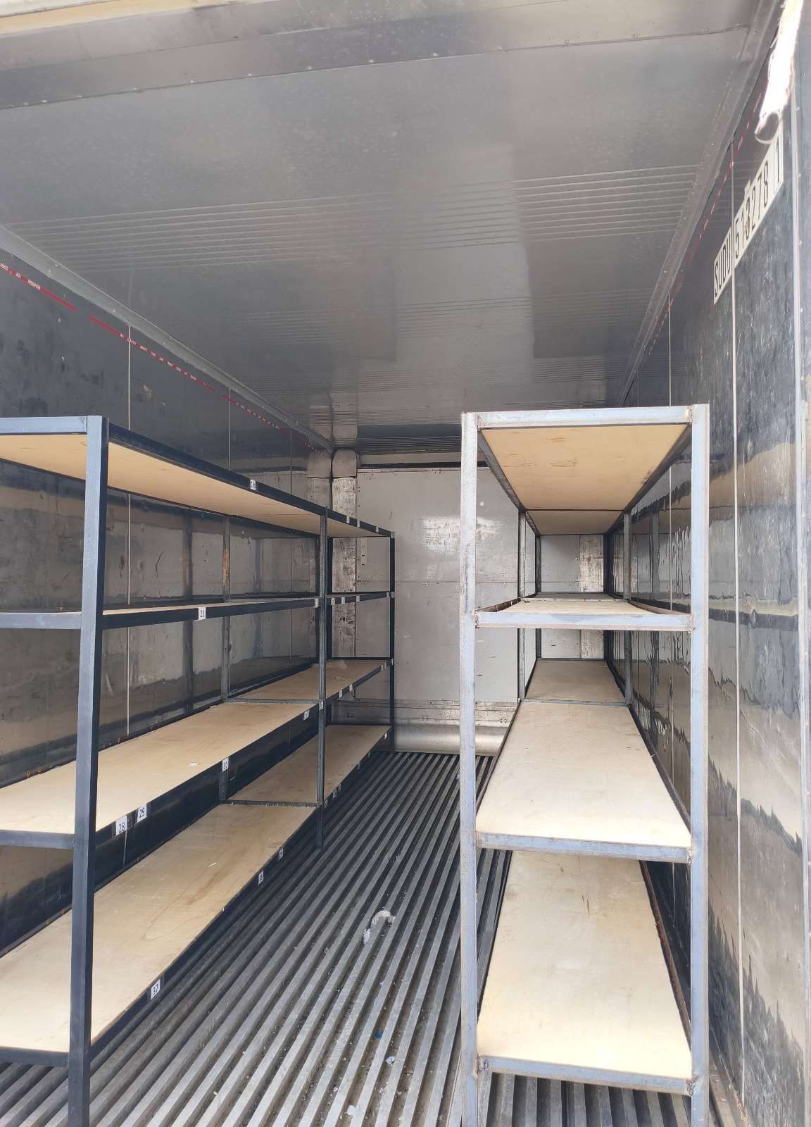 Interior do container reefer com estantes metálicas e prateleiras de madeira