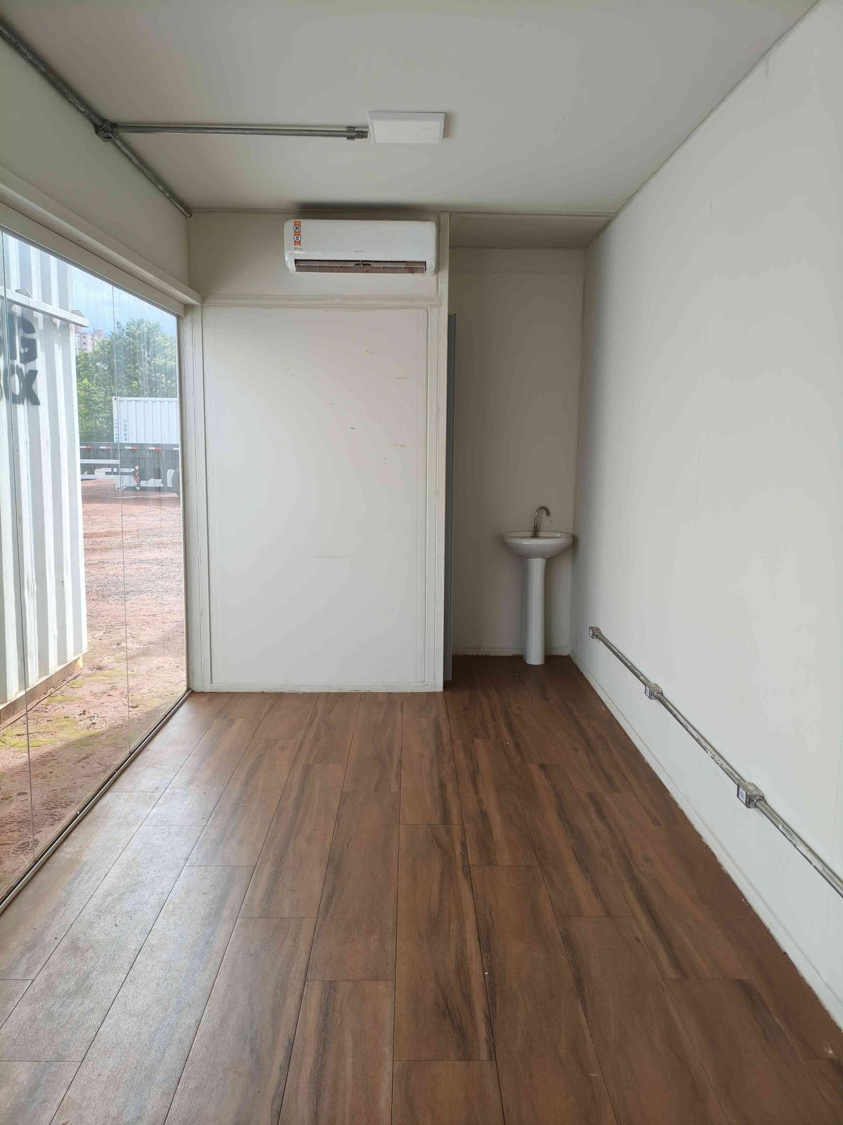 Interior do estande em container com piso amadeirado, ar-condicionado e banheiro ao fundo