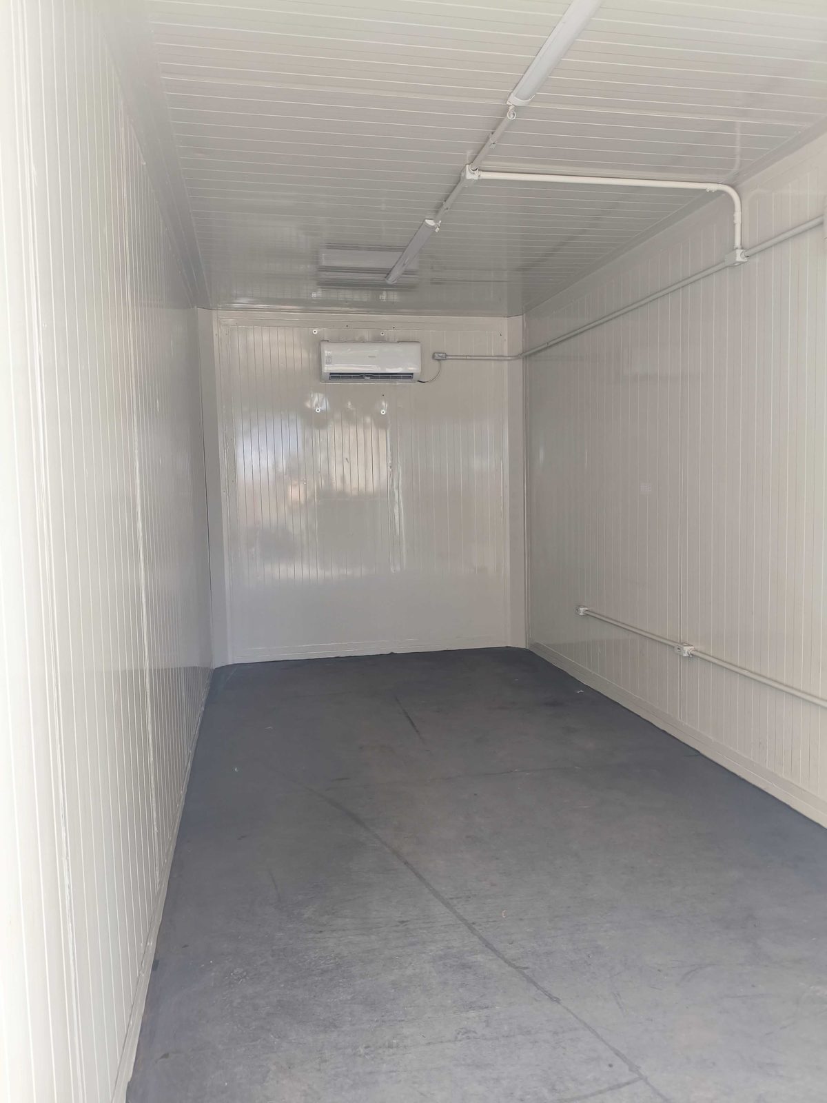 Interior do container escritório climatizado com paredes brancas e piso cinza