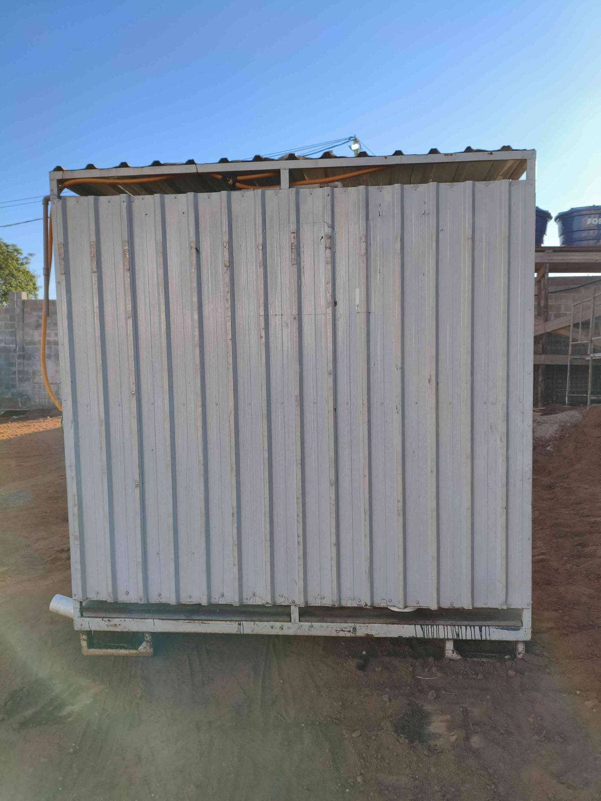 Lateral do container banheiro sobre terreno de terra vermelha na obra